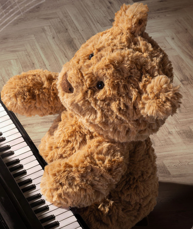Cute Bartholomew Bear teddy plush sitting beside piano, soft cuddly stuffed bear