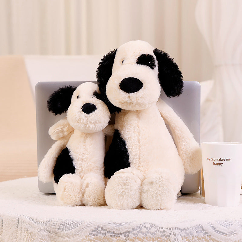 Two sizes of bashful black & cream puppy plush toys on table, cute spotted stuffed dog companion